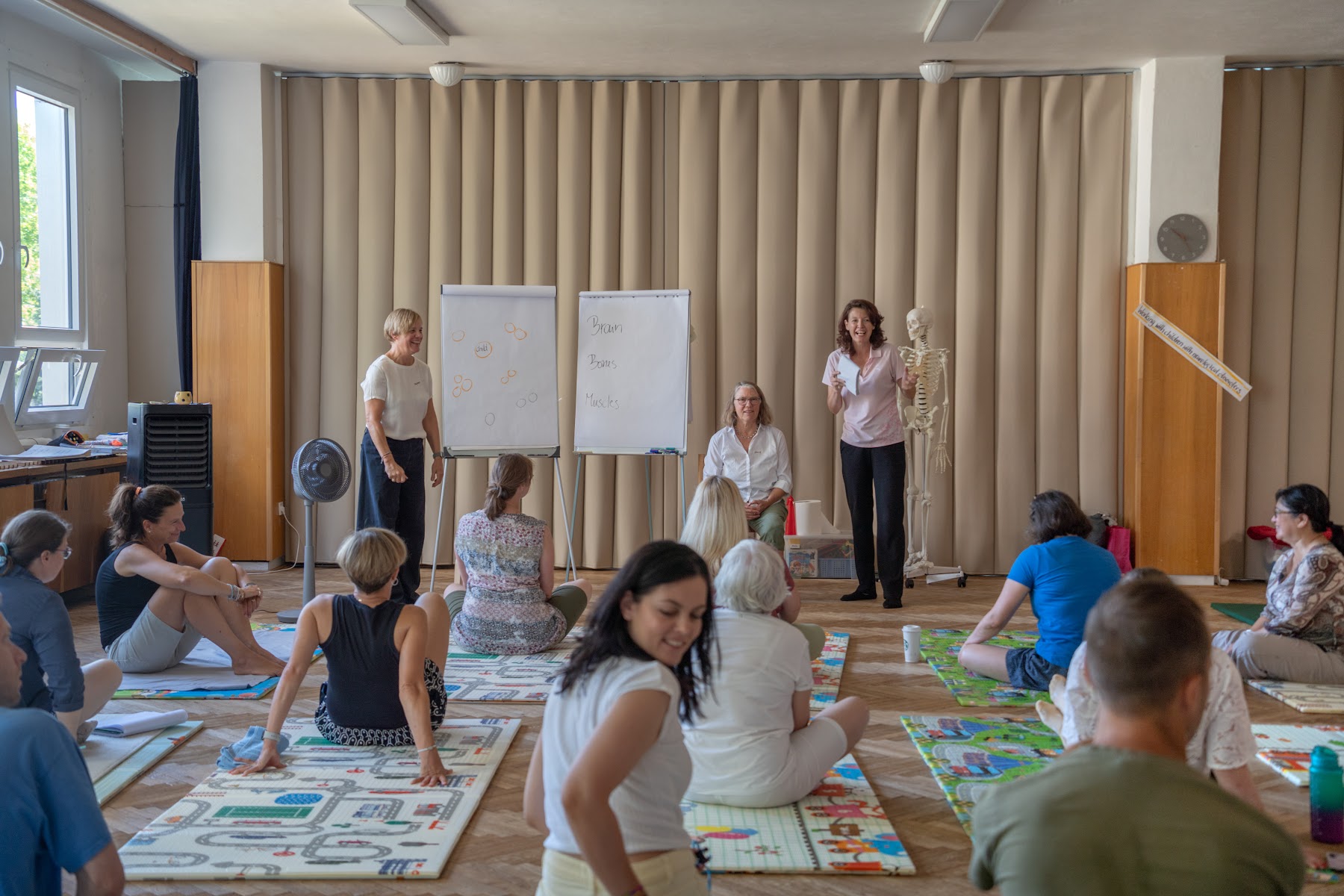 Účastníci se při pohybové lekci otáčejí v sedu na podložkách